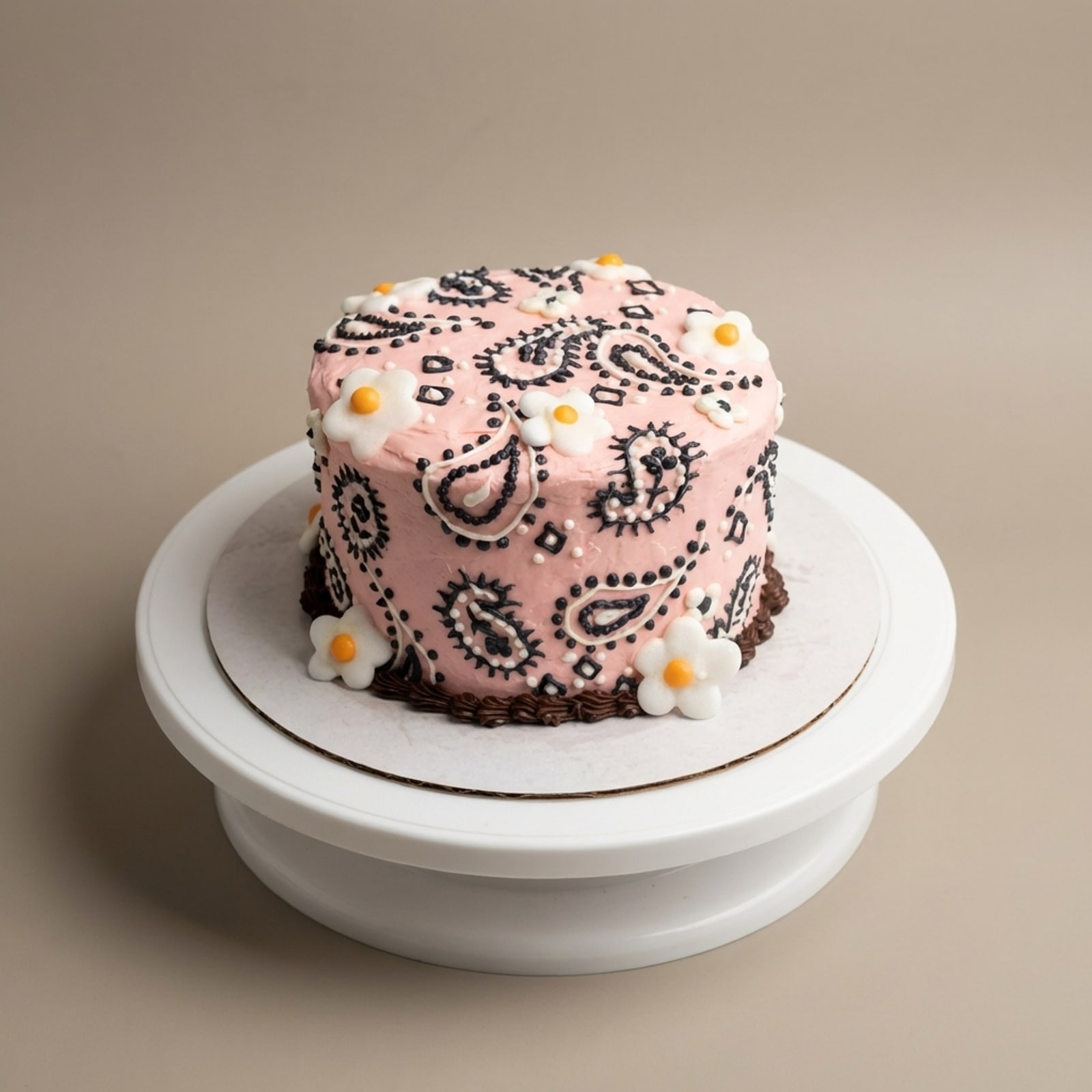 Side view of a blush pink buttercream cake with paisley piping, white floral accents, and scalloped chocolate base trim.